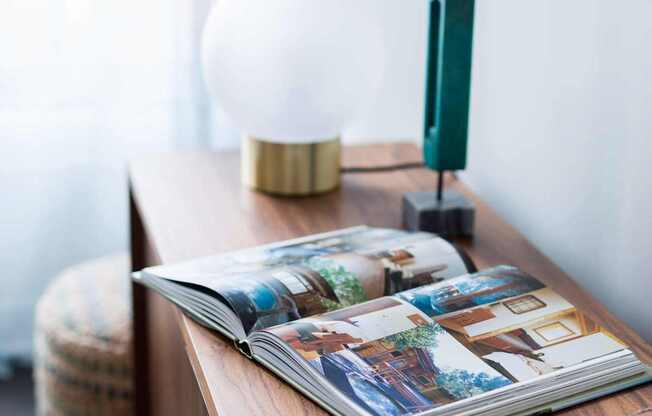 A magazine is open on a wooden table with a lamp and a green object beside it at The Pennsylvanian Apartments, Pennsylvania