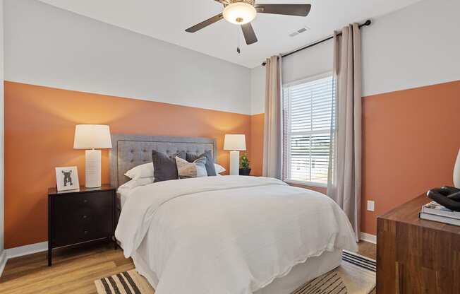 a large bedroom with a ceiling fan, accent wall, and model furnishings