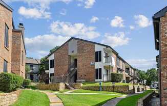 An apartment building with green lawns in front at The Oaks of Denton Apartments in Denton, TX