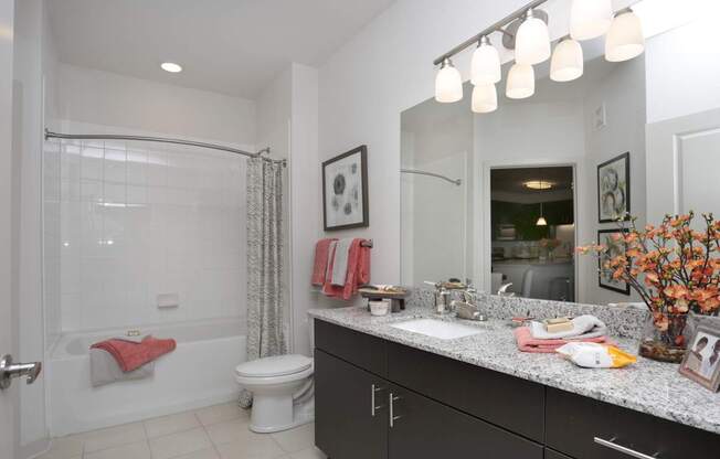 A bathroom with a white toilet, a white bathtub with a red towel, a sink with a mirror above it, and a vase with flowers on the counter.