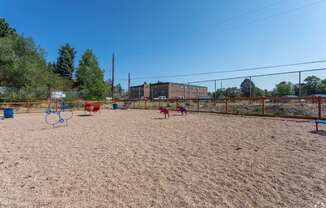 A sandy playground with red and blue swings and a basketball hoop.