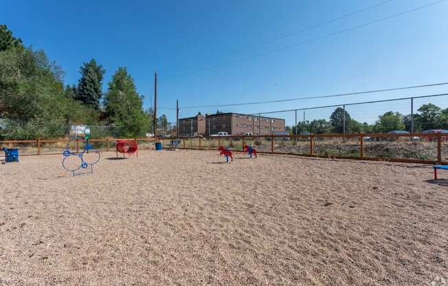 A sandy playground with red and blue swings and a basketball hoop.