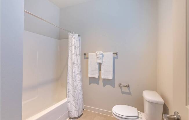 A white toilet sits next to a white shower curtain in a bathroom at Forestplace Apartment Homes, Forest Grove, OR