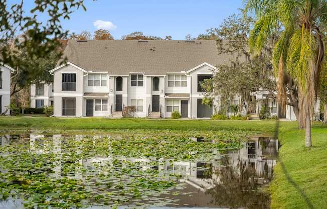 A large white building with a grey roof is reflected in a pond.
