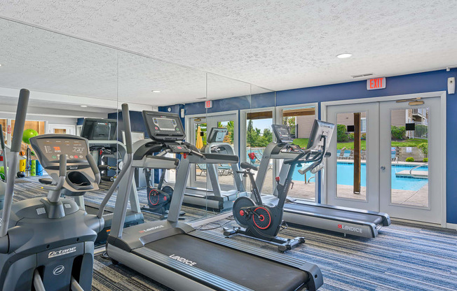 a gym with cardio machines and a pool in the background