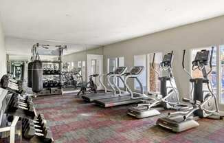 a spacious fitness room with cardio equipment and windows