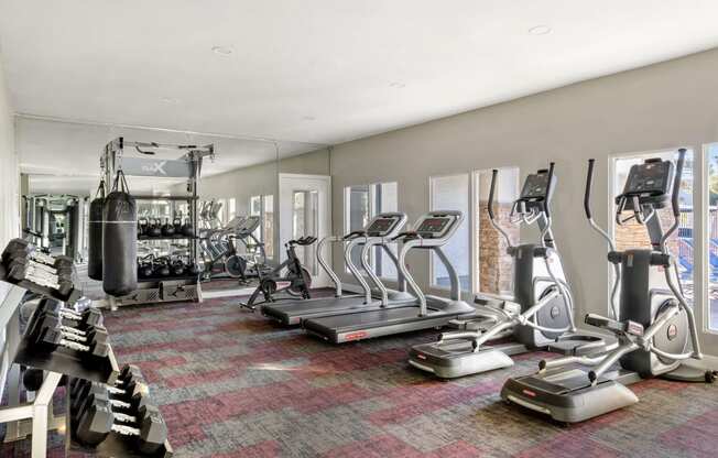 a spacious fitness room with cardio equipment and windows