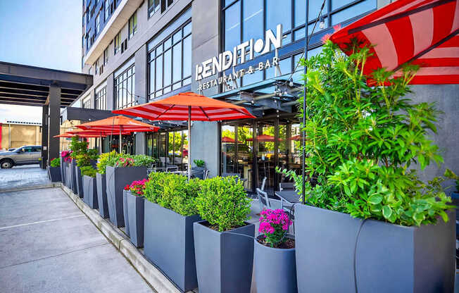 A row of grey planters with greenery and flowers in front of a building with a red and white striped awning.