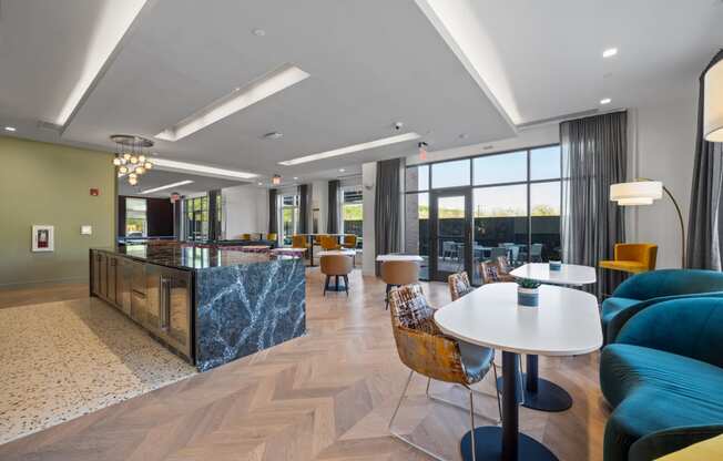 A community kitchen and resident lounge with a long bar, tables, chairs, and large windows.
