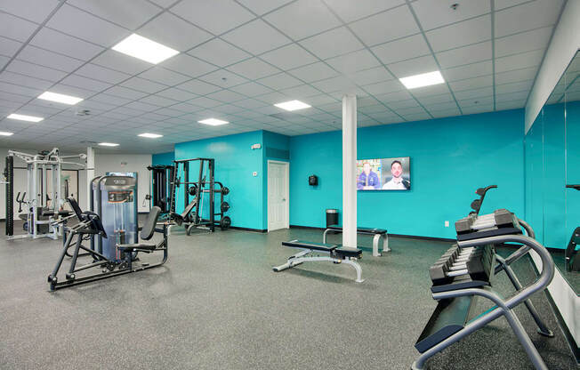 a gym with weights and cardio equipment and a tv at Presidio Palms Apartments, Tucson