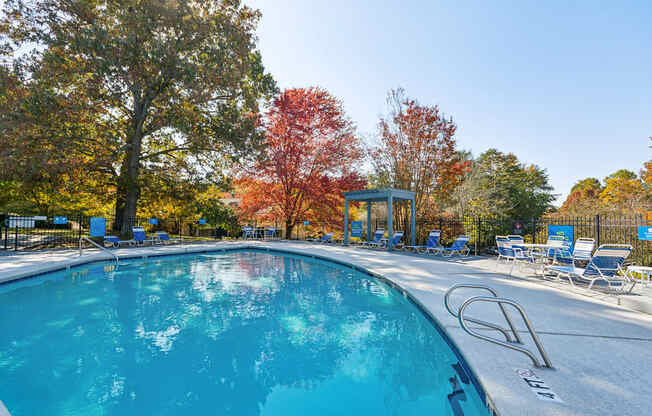 a swimming pool with chairs and trees in the background