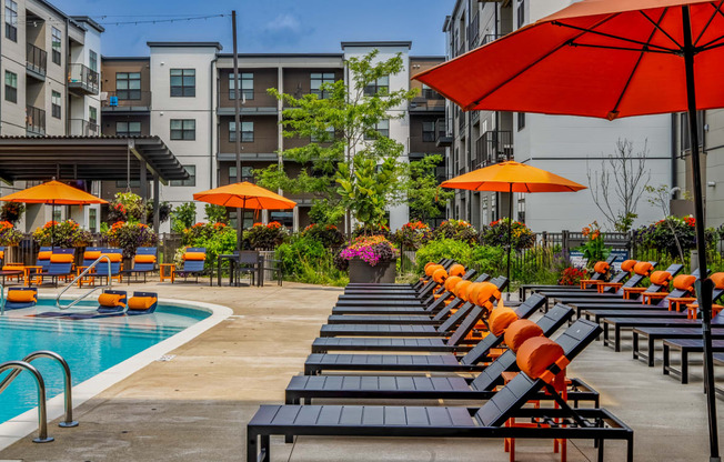 a pool with lounge chairs and umbrellas at an apartment complex