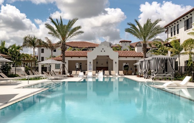 a resort style swimming pool with white lounge chairs and palm trees