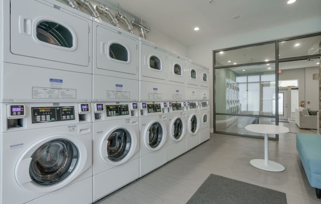 a spacious laundry room with white washers and dryers and a white table with a blue