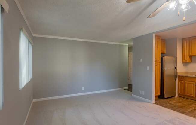 an empty living room with a refrigerator and a kitchen