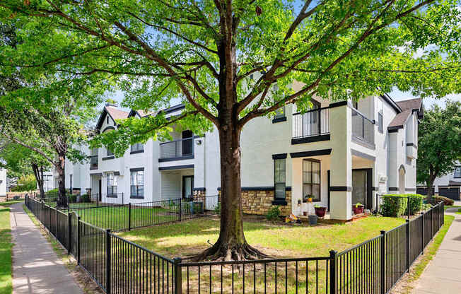 Apartment exterior with fenced yard, private patio, balconies, and mature shade tree.