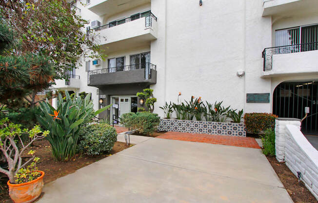 an apartment building with a sidewalk and plants in front of it