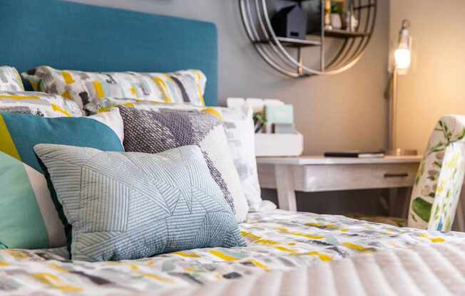 A bed with a blue headboard and a white desk in the background.
