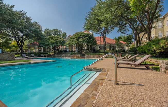 A swimming pool surrounded by trees and lounge chairs.