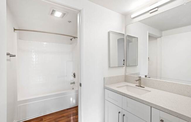 A white bathroom with a sink, mirror, and shower.