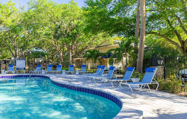 A pool surrounded by trees and chairs.