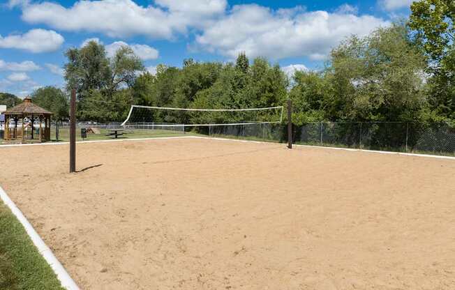 A sandy tennis court surrounded by a fence and trees.