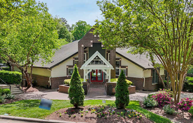 A house with a red door and a small porch surrounded by trees and bushes.