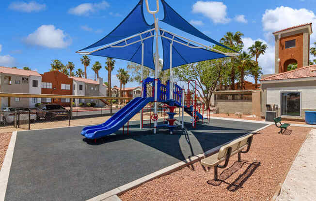 a playground with a blue slide and umbrella at villas at houston levee west apartments