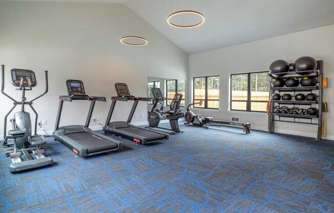 a gym with cardio equipment and weights in a room with windows