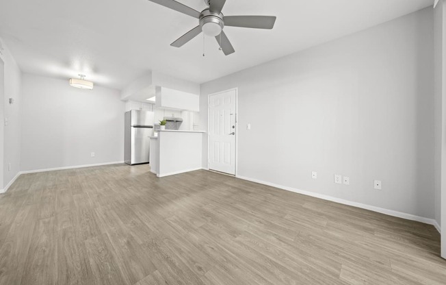 an empty living room with a ceiling fan and a kitchen