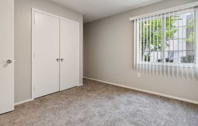 an empty bedroom with a window and a closet