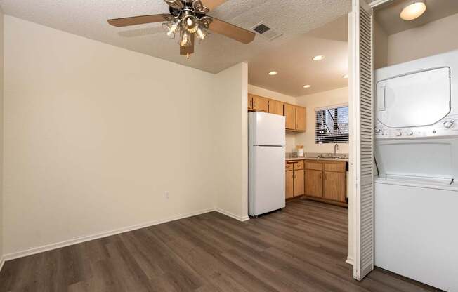 A room with a ceiling fan and a kitchen area with a refrigerator and oven.