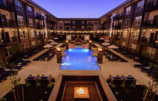 A large outdoor pool surrounded by lounge chairs and umbrellas in a courtyard.