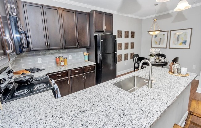 U-shaped kitchen with dark wooden cabinets and speckled countertops leading into the dining room