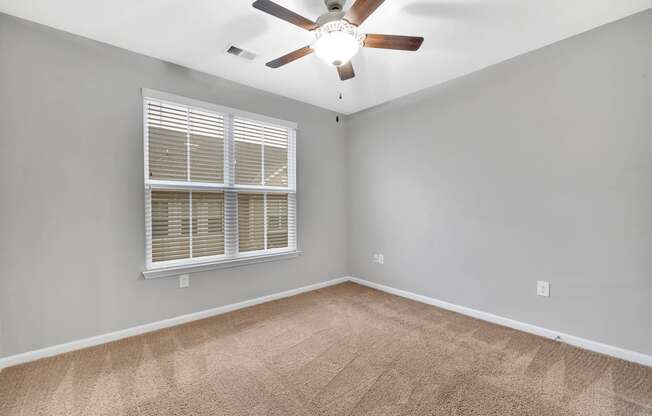 an empty living room with a large window and a ceiling fan