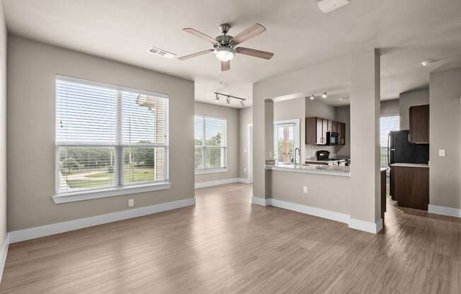an empty living room with a ceiling fan and a kitchen