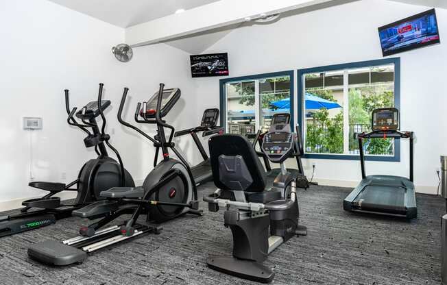 a gym with various cardio equipment in a room with windows