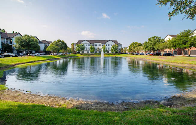 a fountain in the middle of a pond with apartments in background