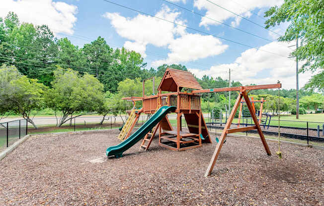 A playground with a green slide and a wooden swing set.