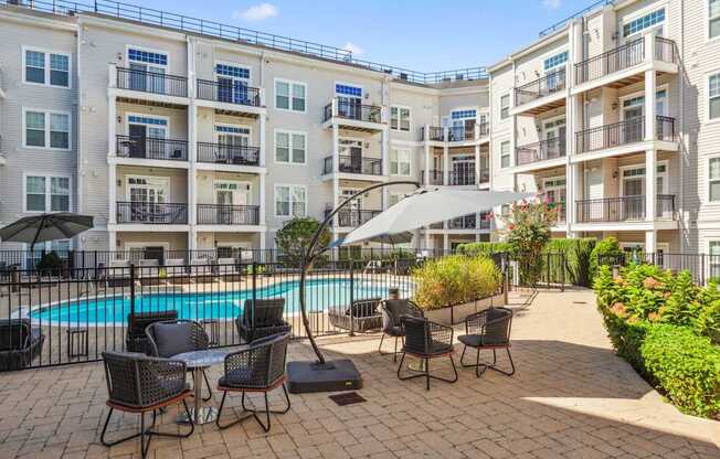A pool surrounded by chairs and umbrellas in front of apartment buildings.