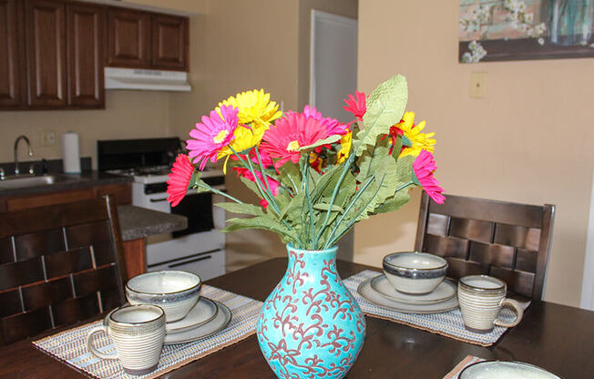 a vase of flowers on a table with plates and cups