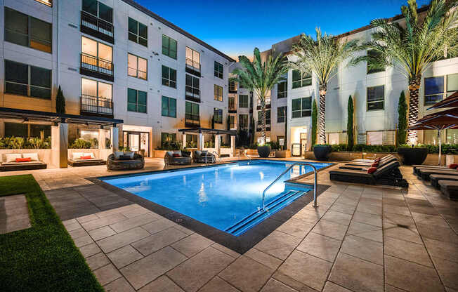Tranquil pool surrounded by private cabanas, woven lounge chairs, and glowing palm trees
