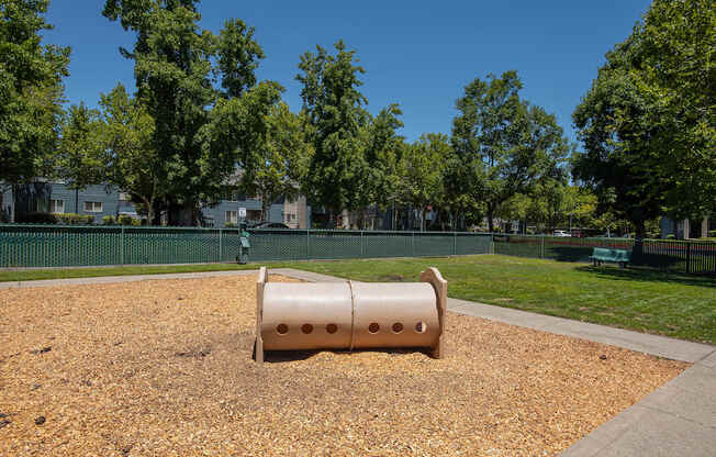 A dog park with a beige cylinder and bark dust at Autumn Oaks Apartments, Roseville, CA, 95678