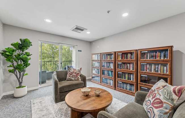 A living room with a grey couch, a wooden coffee table, a green plant, and a bookshelf filled with books.