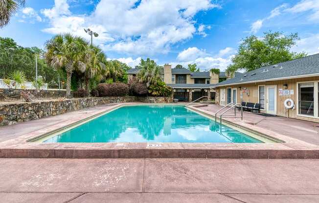 A swimming pool surrounded by a stone wall and palm trees.