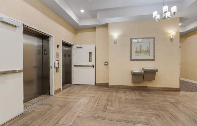 a lobby with two elevators and two urinals and a hallway with doors