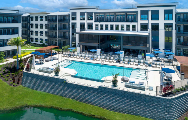 a large pool with lounge chairs and umbrellas in front of a building