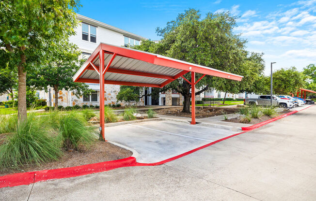 a red covered parking lot with trees and a building in the background