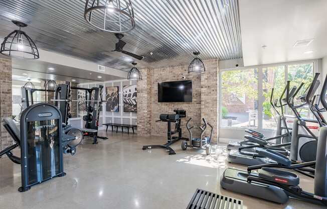A spacious gym with a variety of exercise equipment and a television mounted on the wall.