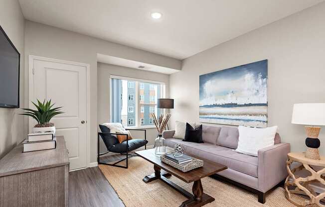 A living room with a grey couch, a coffee table, a chair, a potted plant, and a painting on the wall.